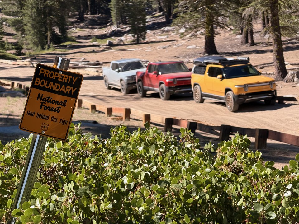 Three Rivians parked beyond a National Forest property boundary sign