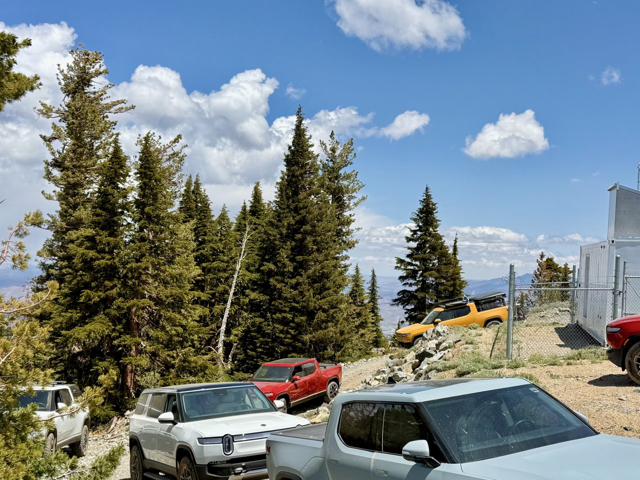 Five Rivians parked along a high trailhead above a wide valley