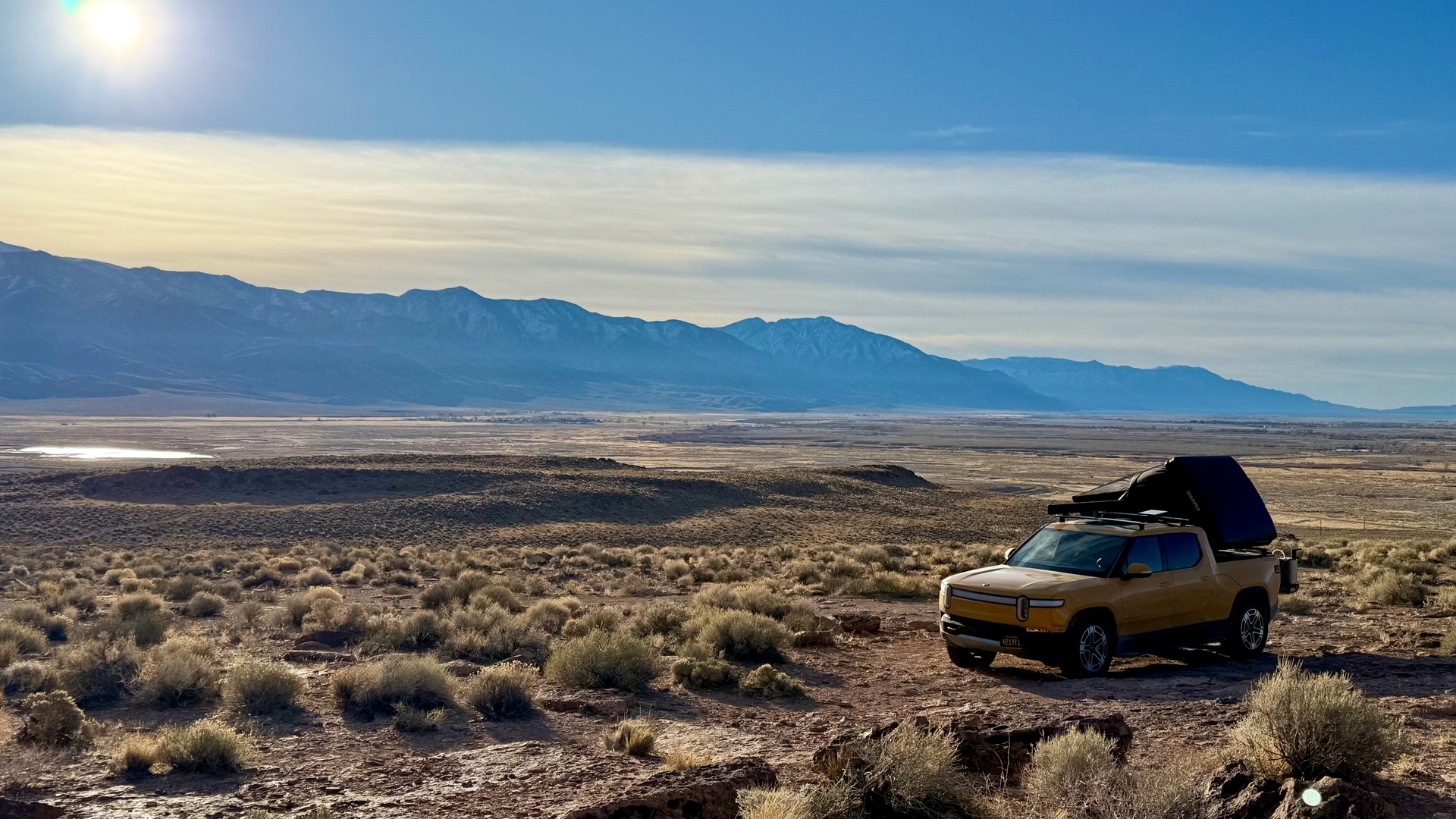 Compass Yellow Rivian R1T with rooftop tent in a broad mountain landscape