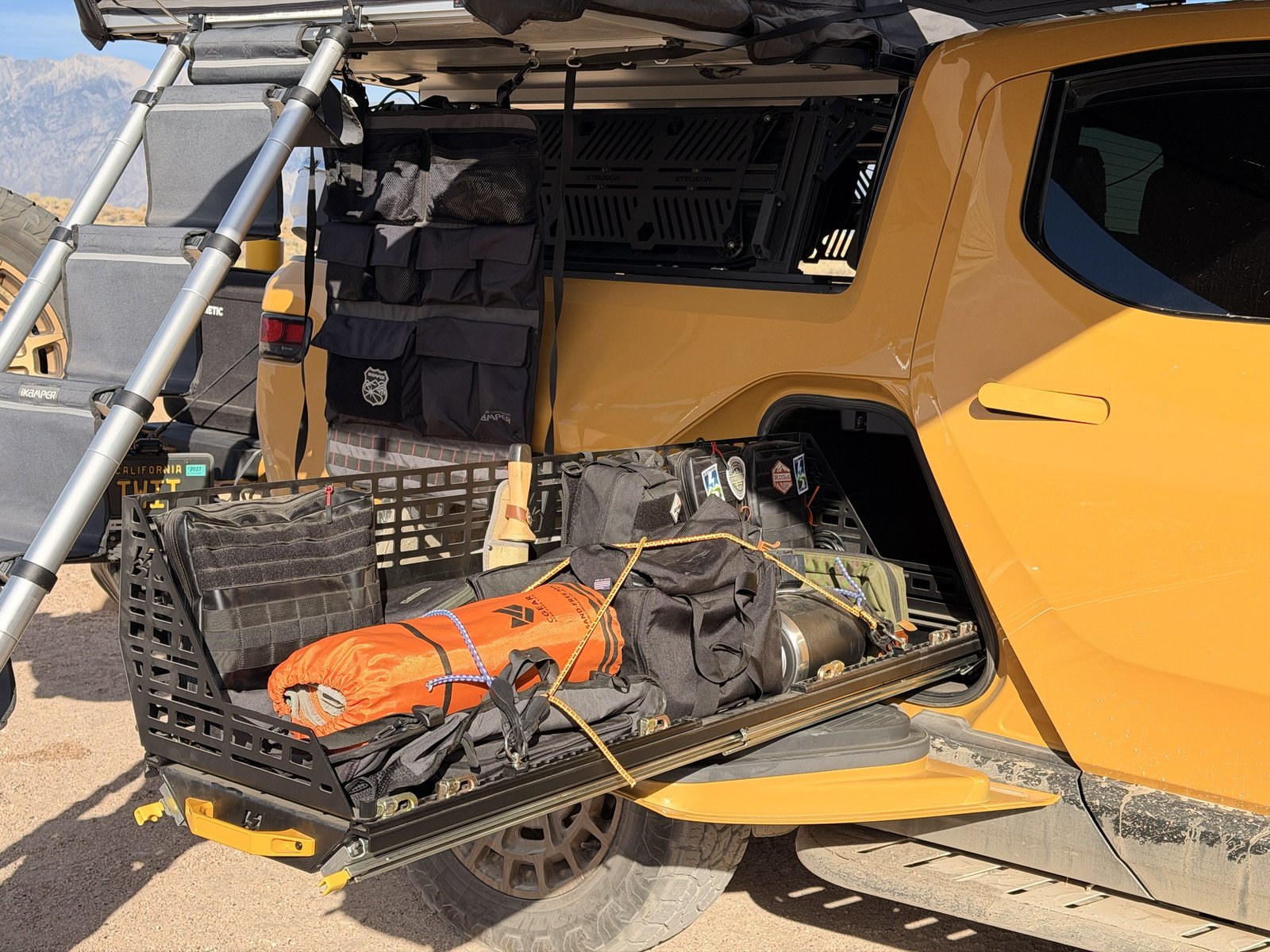 Loaded gear tunnel slide packed with duffels and camp gear behind the Rivian