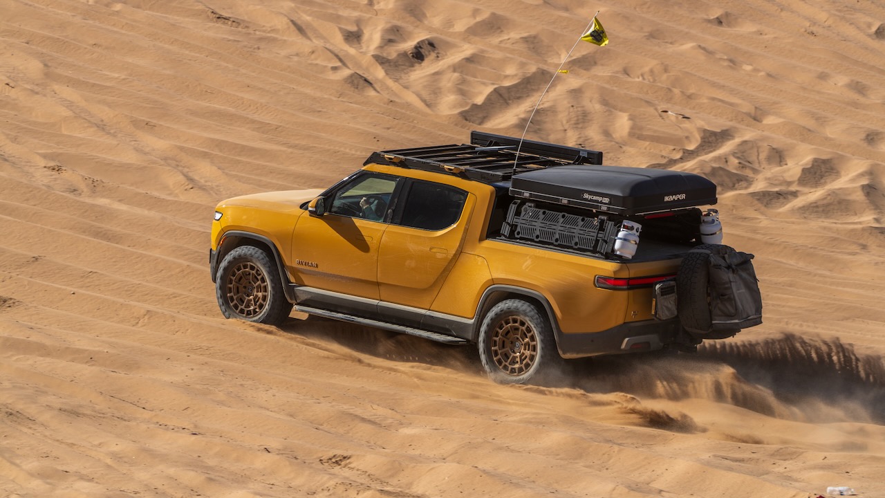 Yellow Rivian R1T driving across desert dunes
